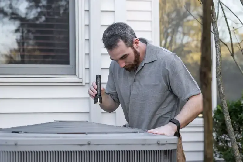 HVAC technician inspecting an outdoor air conditioning unit beside a house